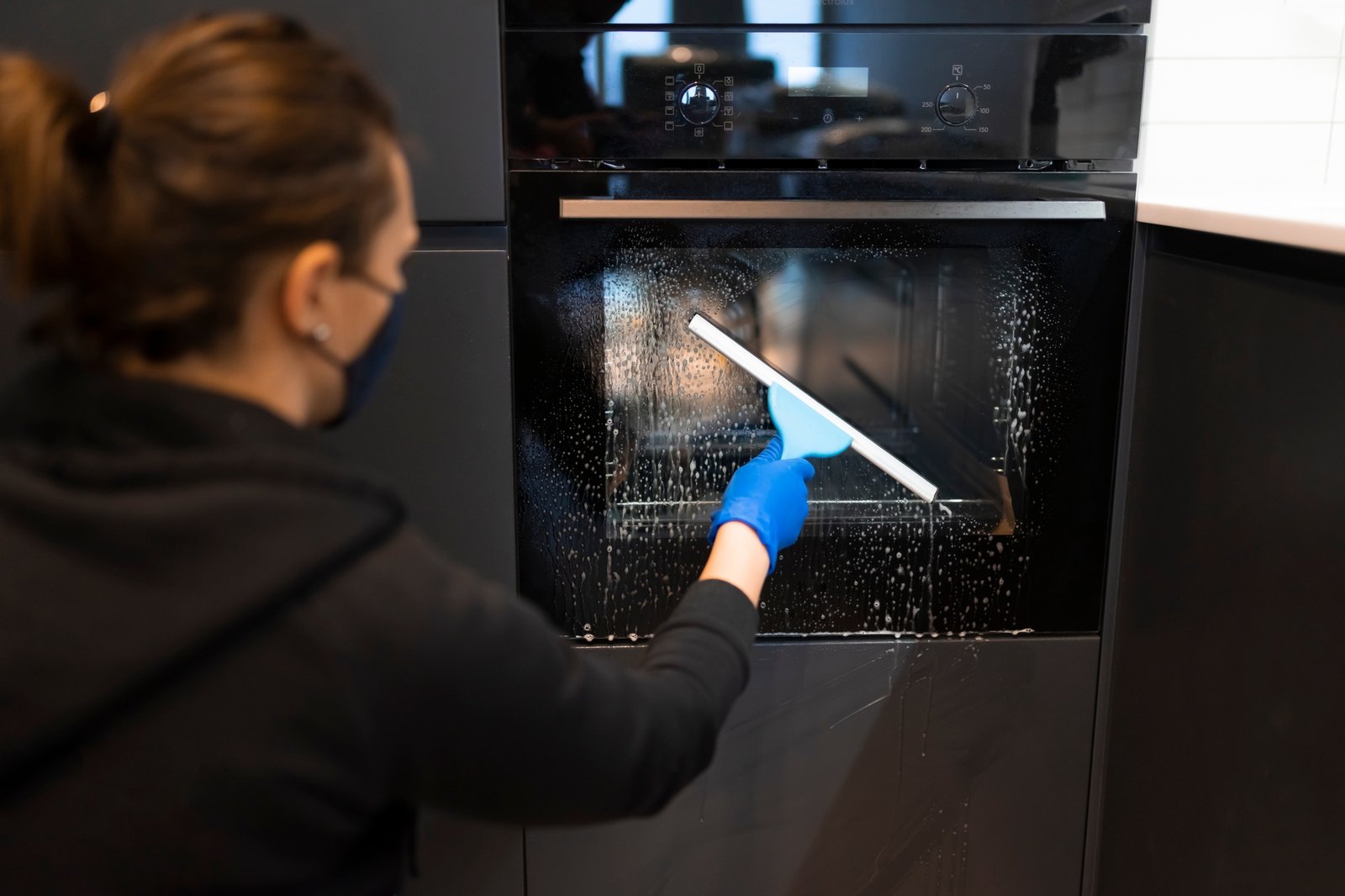 Woman washing the oven. Process of cleaning oven glass with water squeegee