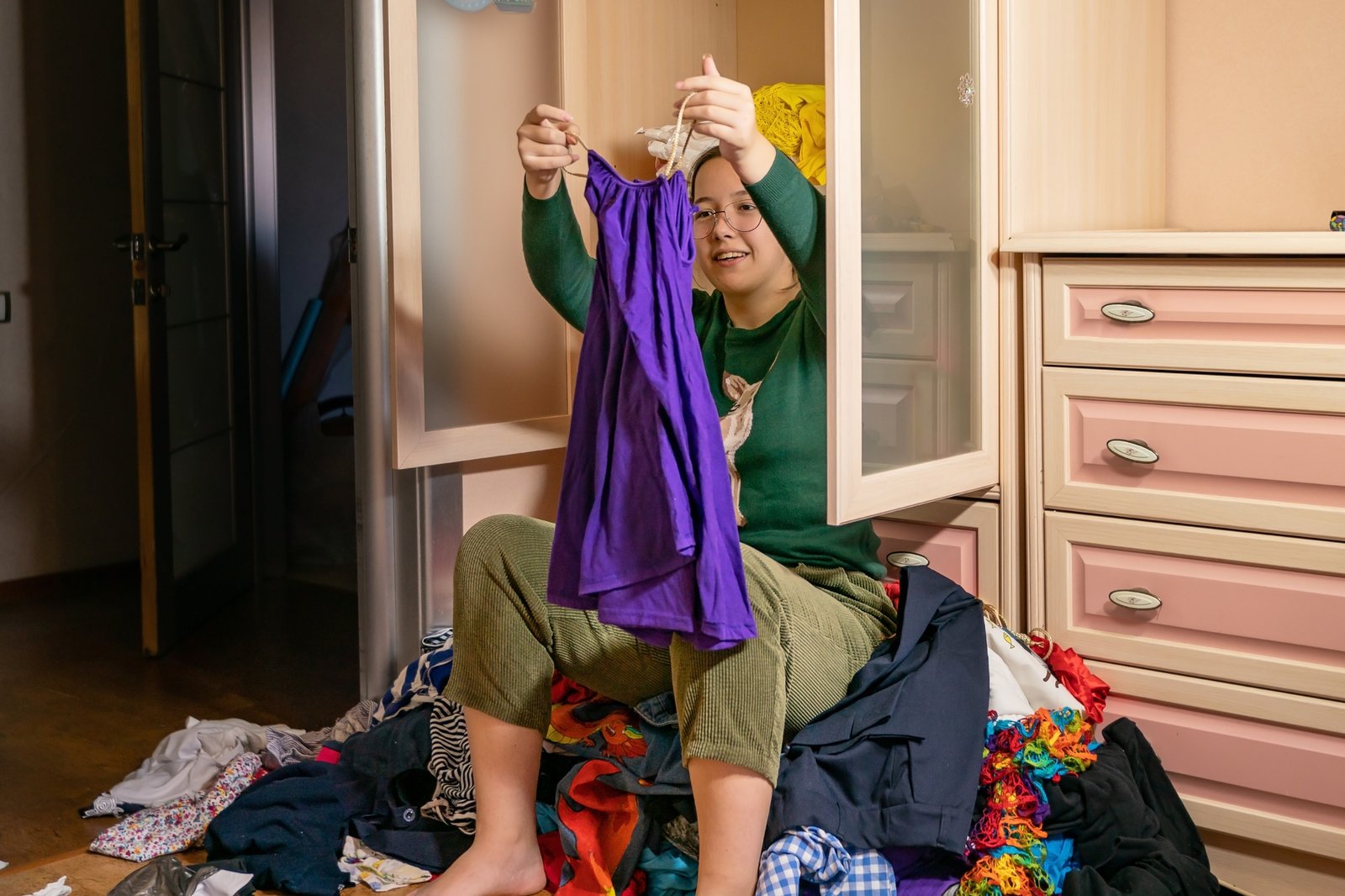 the girl sits on a pile of things thrown out of the cupboard. house cleaning concept